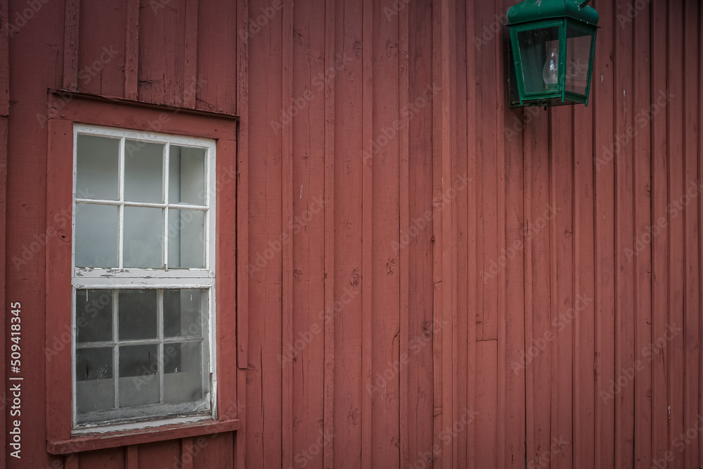 Exterior facade of a wooden barn with a framed glass window and an old lantern hooked on the building
