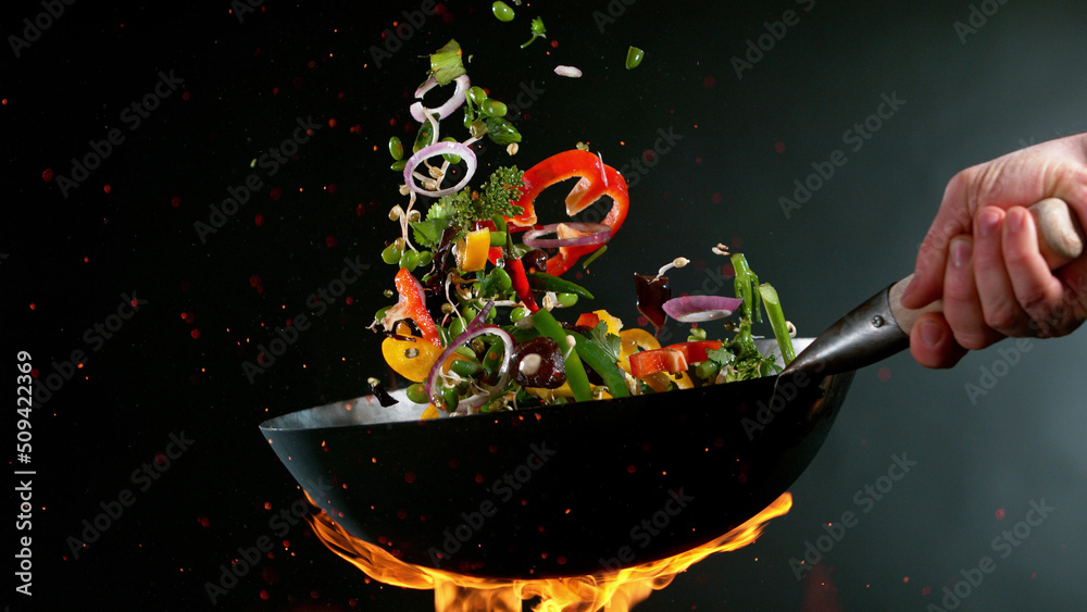 Closeup of chef throwing vegetable mix from wok pan in fire. - obrazy, fototapety, plakaty 