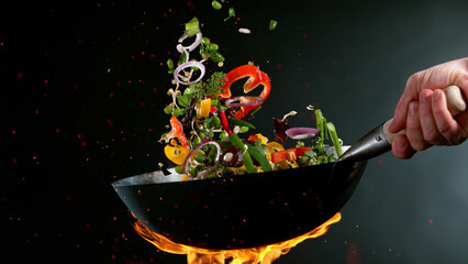 Closeup of chef throwing vegetable mix from wok pan in fire.