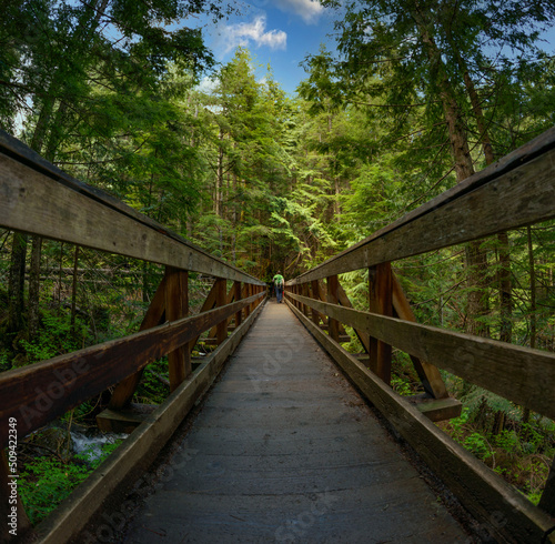 Adventurous athletic male hiker walking across a bridge on a sunny day in the Pacific Northwest. 