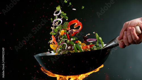 Fotografie, Obraz Closeup of chef throwing vegetable mix from wok pan in fire.