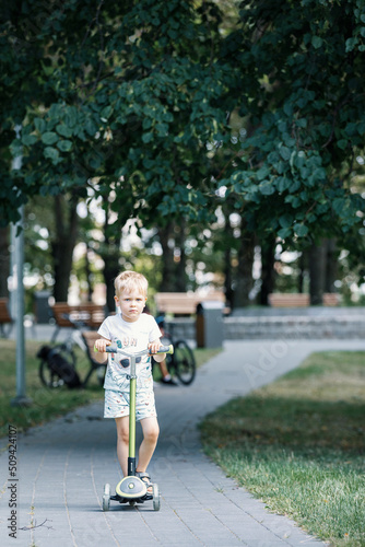 Child on kick scooter in park. A boy is riding on the kick scooter in a park. The concept of a healthy lifestyle. Kids sport.