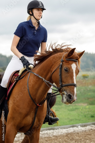 A young girl with a helmet rides a horse in a riding competition. Portrait up close at high riding speed and horse motion