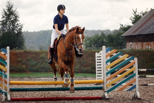 Active woman girl jockey training riding horse jumping over fence. Equestrian sport competition and activity.