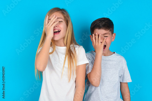 Canvastavla Charismatic carefree joyful two kids boy and girl standing over blue studio background likes laugh out loud not hiding emotions giggling hear funny hilarious joke chuckling facepalm