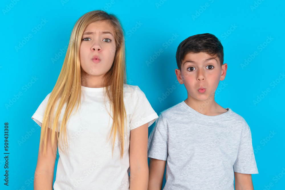 two kids boy and girl standing over blue studio background expressing disgust, unwillingness, disregard having tensive look frowning face, looking indignant with something. two kids boy and girl standing over blue studio background expressing disgust, unwillingness, disregard having tensive look frowning face, looking indignant with something.