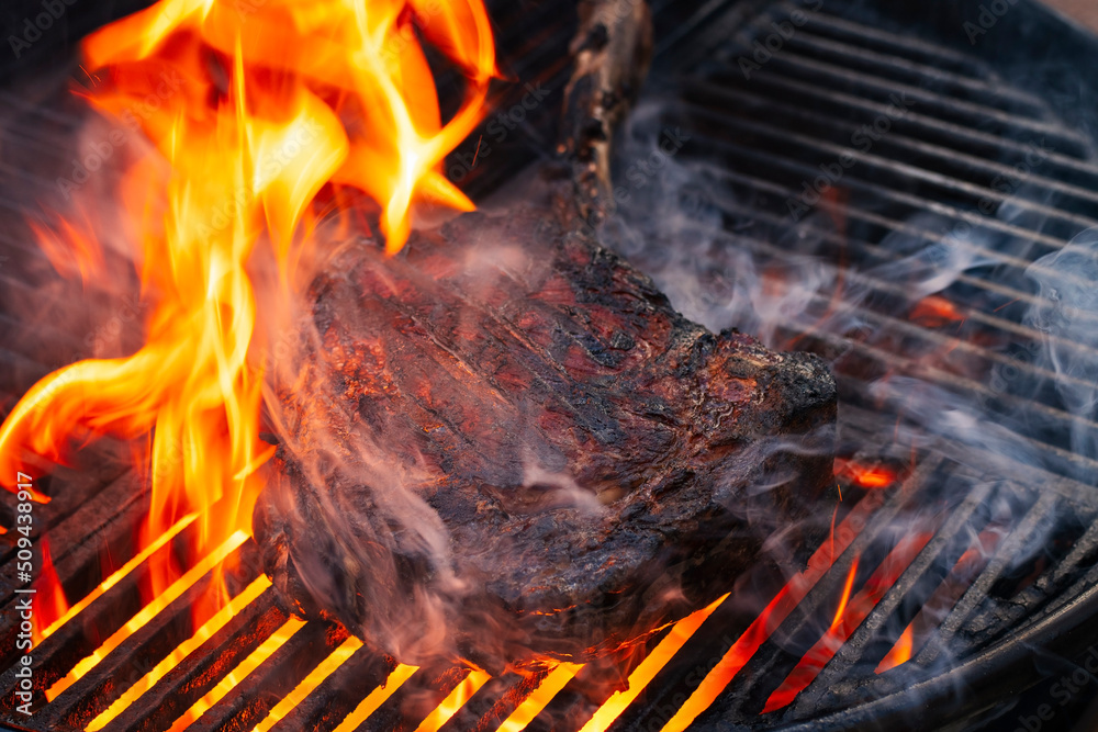 Fototapeta premium Barbecue dry aged wagyu tomahawk steak offered as close-up on a charcoal grill with fire and smoke