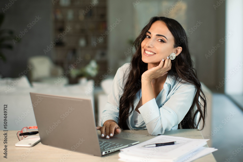 Smiling successful female using laptop computer indoors at home office, making notes on papers, remote work and small business freelancer, education and student, self employed Smiling successful female using laptop computer indoors at home office, making notes on papers, remote work and small business freelancer, education and student, self employed