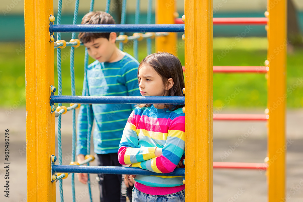 Obraz premium Sad and bored girl and boy stand among the yellow colorful playground, in the park