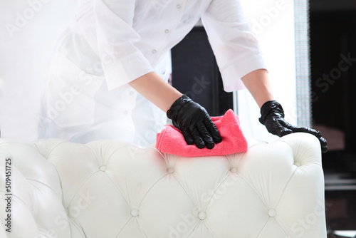 A housewife in black gloves does her homework. A woman wipes dust from a white leather sofa. Leather furniture. Cleaning the apartment.