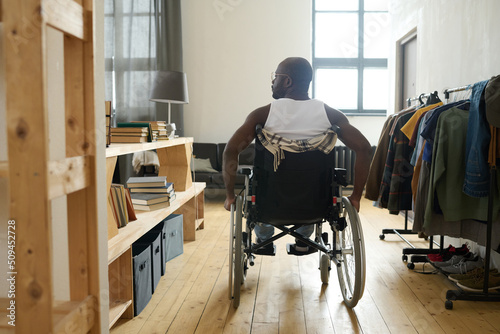 Obraz na plátne Rear view of African man with disability riding along the room on his wheelchair