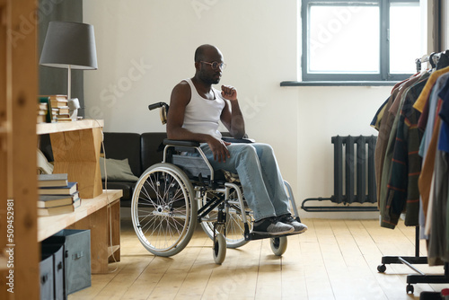 African young man sitting in wheelchair in the room and learning to live alone with disability