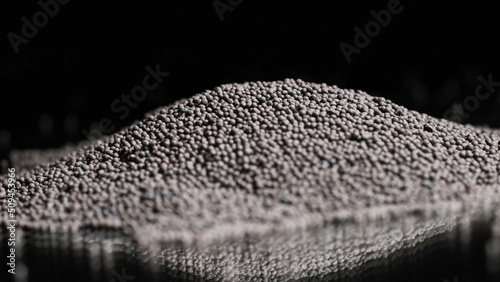 Close-up of gray round grains on black background. Stock footage. Gray round grains for seasoning or decoration on isolated background