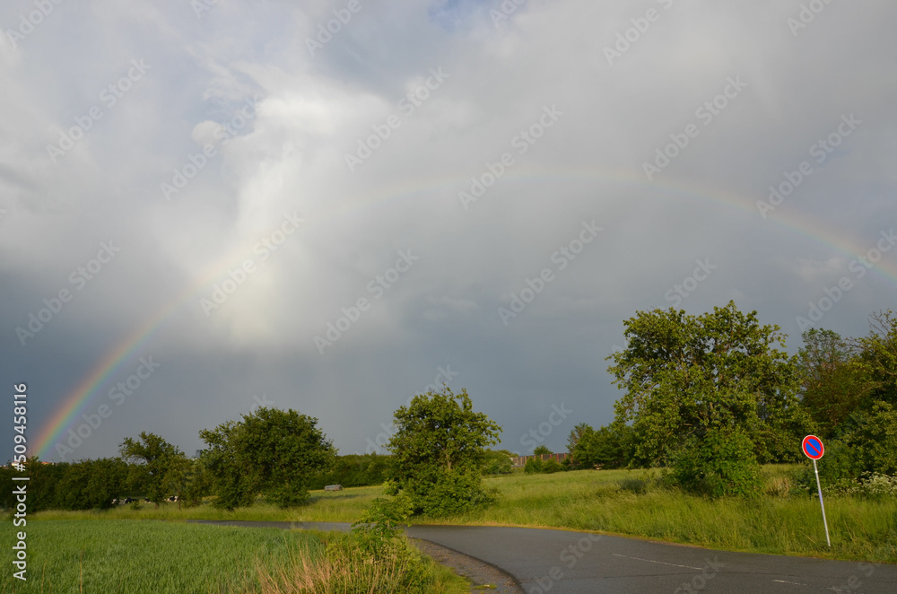 Regenbogen in Frühlingslandschaft mit Sonne und Regenwolken 
