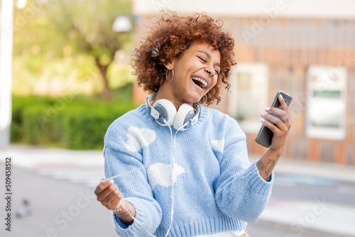 smiling girl looking at mobile phone playing with headphone cable