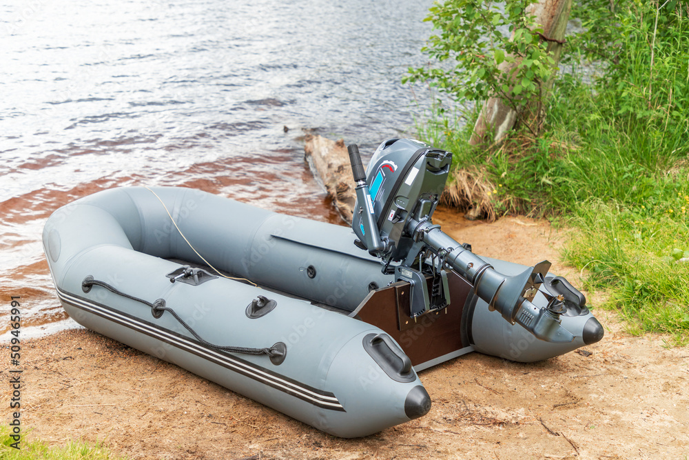 Naklejka premium Empty inflatable boat with motor on shore of lake or river. Water transport for hobby or fishing.