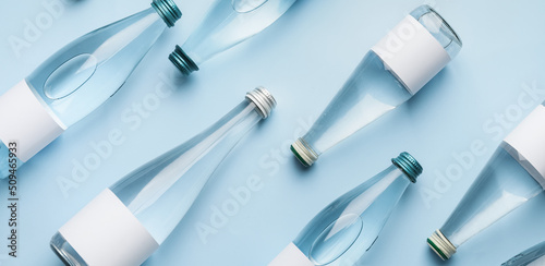 Many bottles of clean water on light blue background, flat lay photo