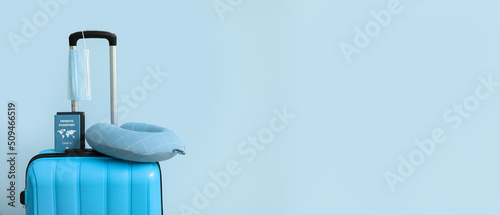 Packed suitcase with immune passport, medical mask and travel pillow on light blue background with space for text