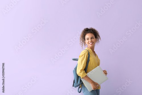 Smiling young African-American woman with laptop on lilac background