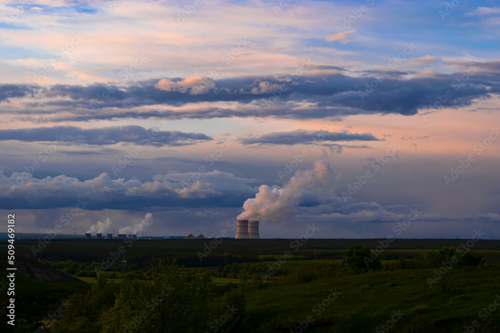 Evening sunset sky scene with dramatic clouds. A nuclear power plant in a field behind a forest