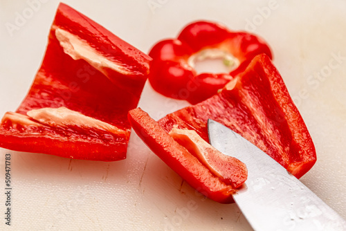 Close up view of a red bell pepper cut in half. The seeds are in the pepper on a cutting board. A knife is in the background photo