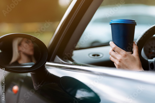cropped photo of woman's hand holding blue paper cup of coffee in car. Hot drink take away. Travel with coffee. Concept of coffee with you. Mockup