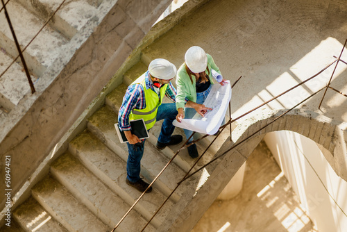 Woman architect explaining blueprint to supervisor at construction site. Engineer talking to contractor.