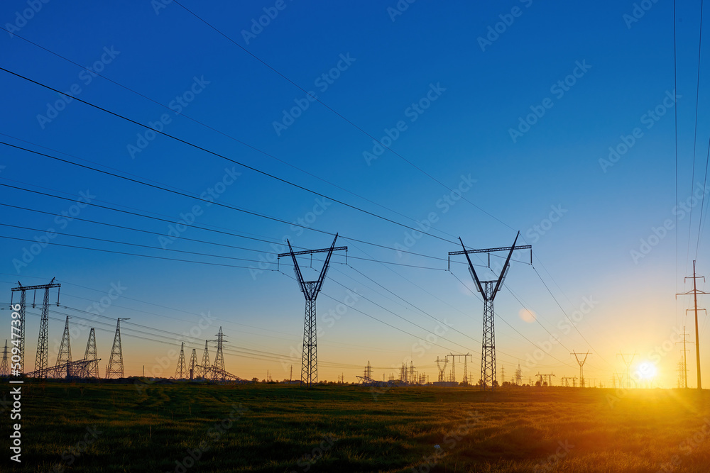 Sun rise on field with high voltage electricity towers. Dark silhouettes of repeating power lines on sunrise. Electricity generation, transmission, and distribution network. Industrial landscape.