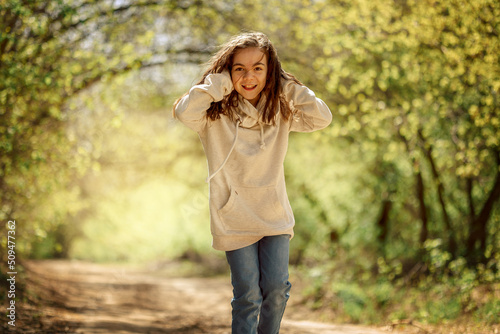 Little pretty girl on walk in sunny spring park. Fairy forest. Child with long hair listens to music, sings, smiles and rejoices. High quality photo