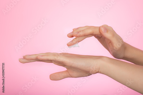 Woman's hand apply hand care cream, isolated on pink background. Female hands using cosmetic cream. Hydrating and moisture soft face or hand cream - skin care concept. Selective focus, close up