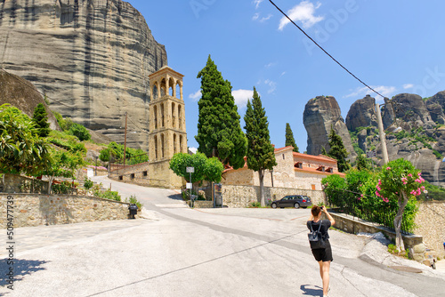 a tourist walking and takes pictures on a smartphone near the bell tower of Byzantine Church of the Assumption of Virgin Mary in Kalabaka, Greece.