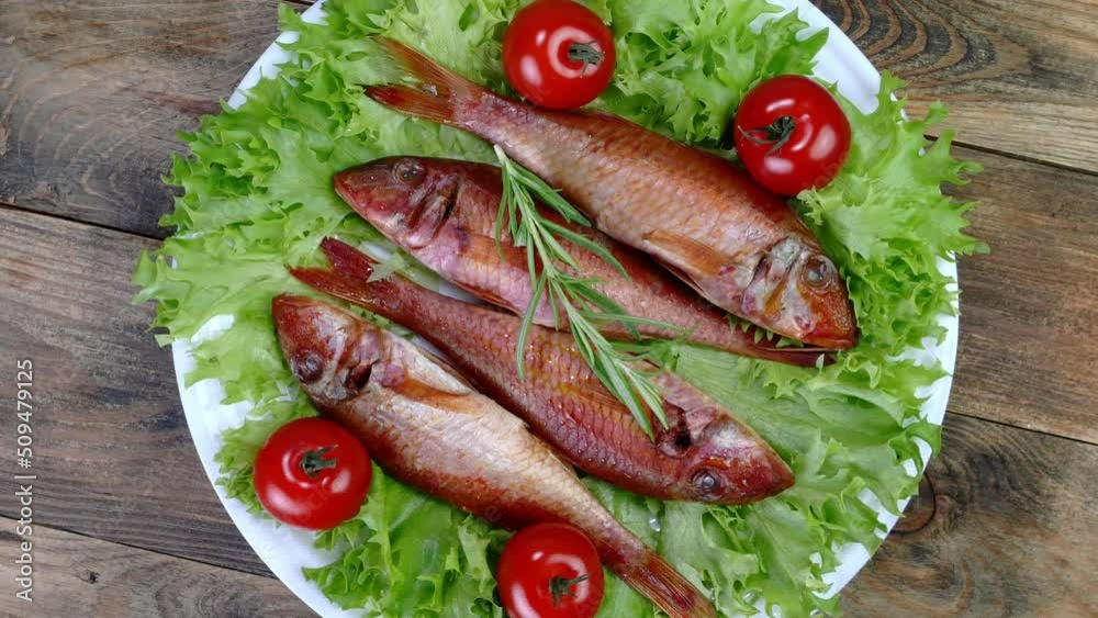 Smoked whole sea fish served salad leaves with tomato and rosemary rotate slowly on white dish. Smoked whole sea fish served salad leaves with tomato and rosemary rotate slowly on white dish.