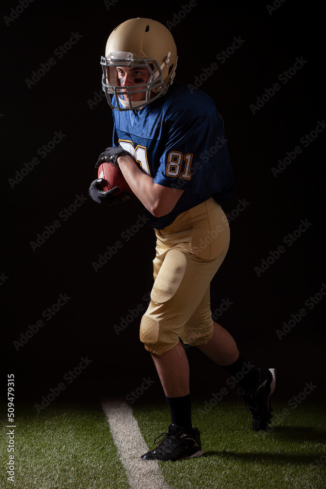 Full length view of football player running with the ball on grass field and dark background