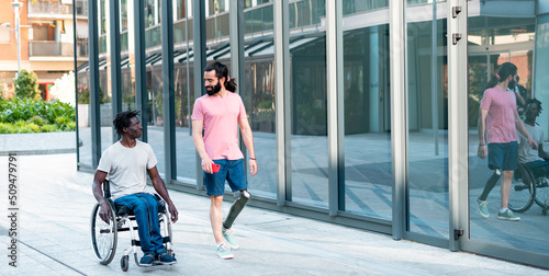 Multiracial friends walking in a disability friendly city - Two adult man speaking and walking in the street with modern building  as background