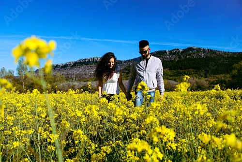 vertical portrait of a young couple walking hand in hand through a field of flowers on a sunny day