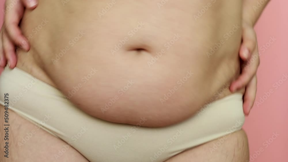 Cropped shot of fat woman with overweight wiggling and moving. Excessive fat on stomach. Concept of reducing abdomen. Pink background. Subcutaneous fat breakdown. Burning visceral fat, calories