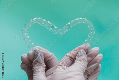 Hands holding dental aligners in heart shape on blue background