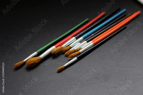 Different painting brushes on black blurred background, horizontal photo. Various sizes and colors of artist's tools, dry clean brushes for watercolor