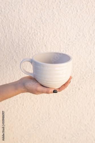 hand with painted nails holding a white handmade ceramic cup