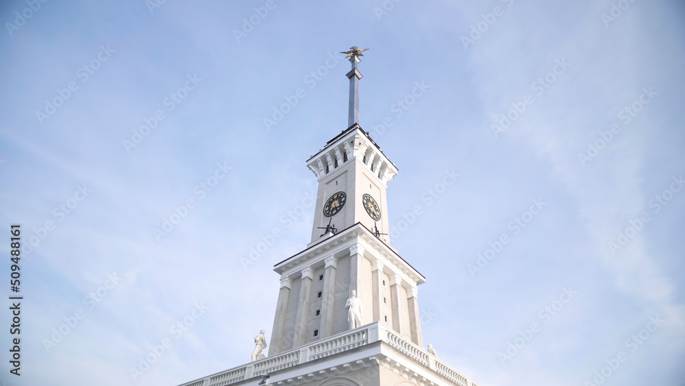 White clock tower on background of blue sky. Action. Bottom view of beautiful white clock tower on background of sky. Clock tower of Northern river station in Moscow