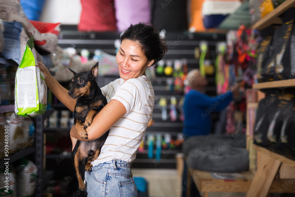 Obraz premium Happy female customer with dog choosing dry food in petshop
