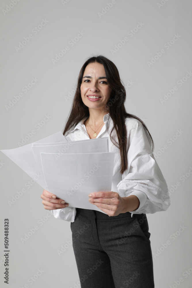 Middle-aged woman, mentor coach stays over white wall holds documents. Middle-aged woman, mentor coach stays over white wall holds documents.