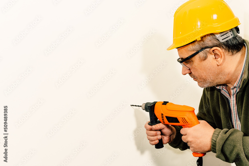 Worker drilling a hole with a drill on a white wall. Copy space. Worker drilling a hole with a drill on a white wall. Copy space.