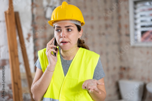 Portrait of young woman builder having telephone conversation in construction site.