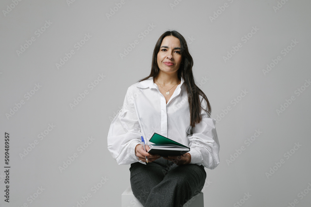 Studio portrait of businesswoman, mentor over white wall writing in notebook. Studio portrait of businesswoman, mentor over white wall writing in notebook.