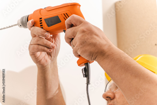 Worker drilling a hole with a drill on a white wall. Copy space.