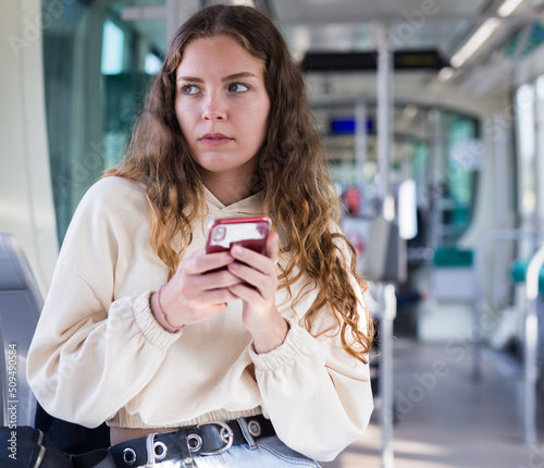 Portrait of a thoughtful girl with a mobile phone in her hands, riding in a tram