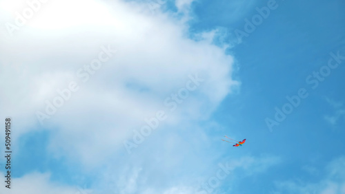Kite flying in the sky among the clouds. Concept. Bottom view of the summer blue sky with white clouds and soaring rainbow colorful kite, concept of freedom and childhood.