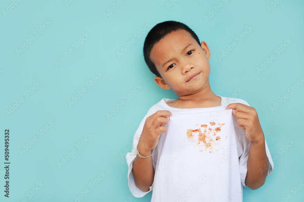 Asian kid showing dirty sauce or food stain on shirt from eating in meal. dirty stain for cleaning concept. Asian kid showing dirty sauce or food stain on shirt from eating in meal. dirty stain for cleaning concept.