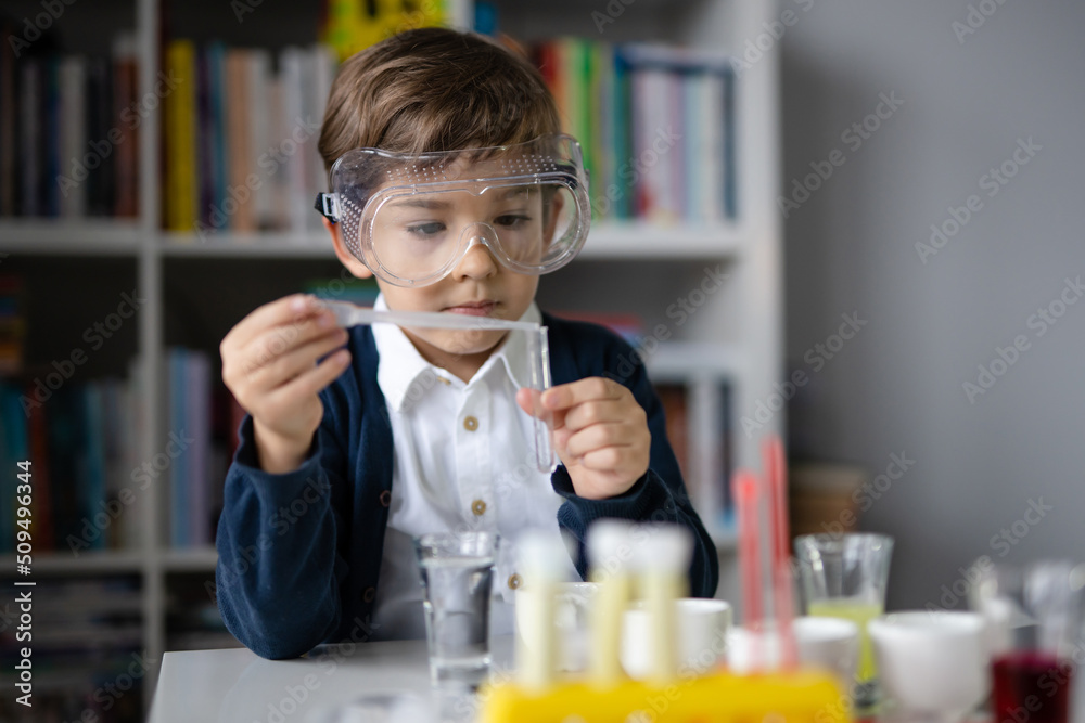 One small caucasian boy scientist five years old wearing protective eyeglasses sitting at the table playing with chemistry equipment toy preforming experiment learning and education concept front view